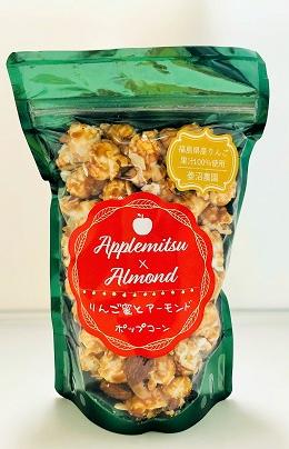 緑色で、前面が透明になっており、中央の赤い丸に商品名がプリントされているチャック付きの袋に入った「フルーツポップコーン（リンゴ蜜とアーモンド）」の写真