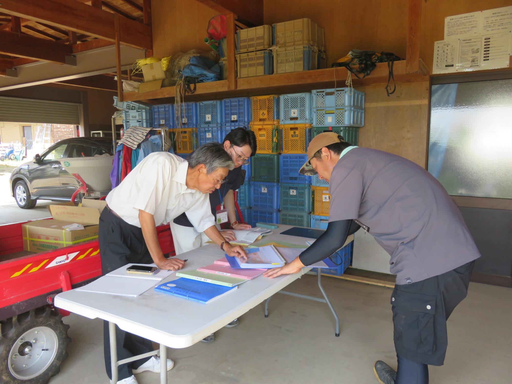 白い机を囲うように3人の男性が立って、書類の確認をしている様子の写真