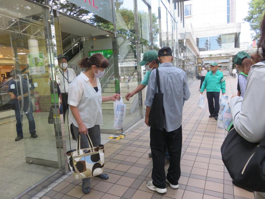 街灯で通行人の男女に交通事故死ゼロを祈念した梨を配布している緑の帽子とシャツを着た男性の写真