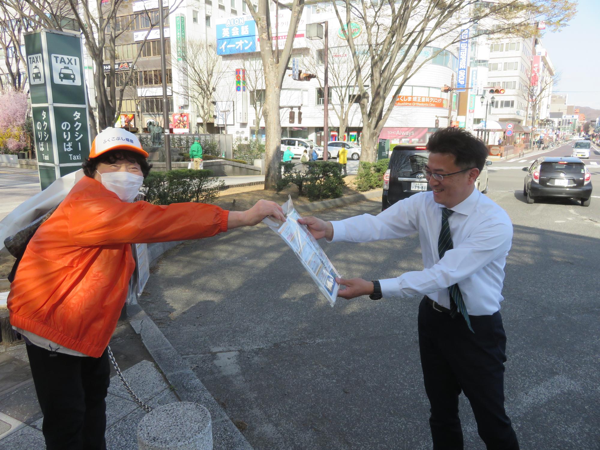 駅前を歩く学生や女性にチラシを配布する警察署職員とキャンペーン参加者たちの写真