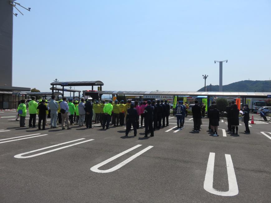 駐車場に警察官や関係団体の人々が大勢集まって整列している様子を後方から写した写真