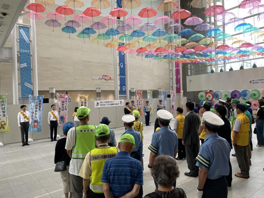 沢山のカラフルなビニール傘が上に飾られたこむこむ館のホールにビブスや帽子を身に着けたたくさんの参加者たちが集まって行われた出動式の様子の写真