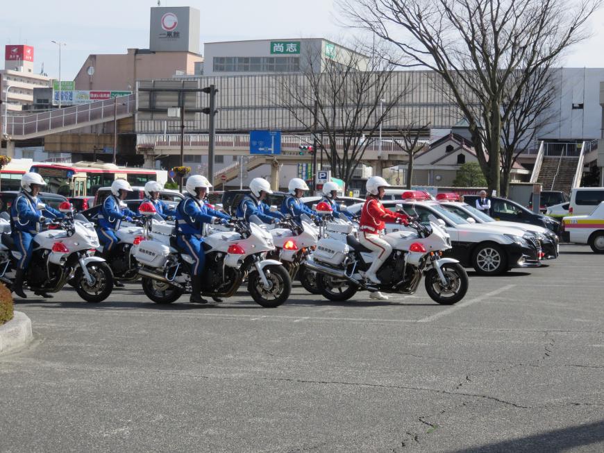 赤い制服の隊員を先頭に青い制服の隊員たちが駐車場に整列した8台の白バイにまたがっている写真