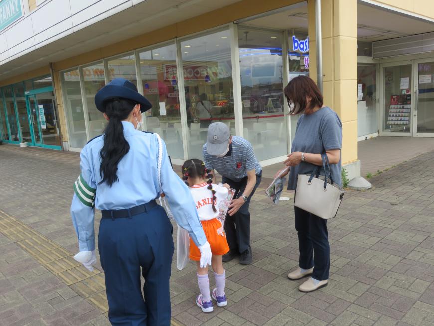 小さな女の子連れの通行人に啓発活動を行う紺色のズボンと帽子、水色のシャツの制服を着た女性の写真