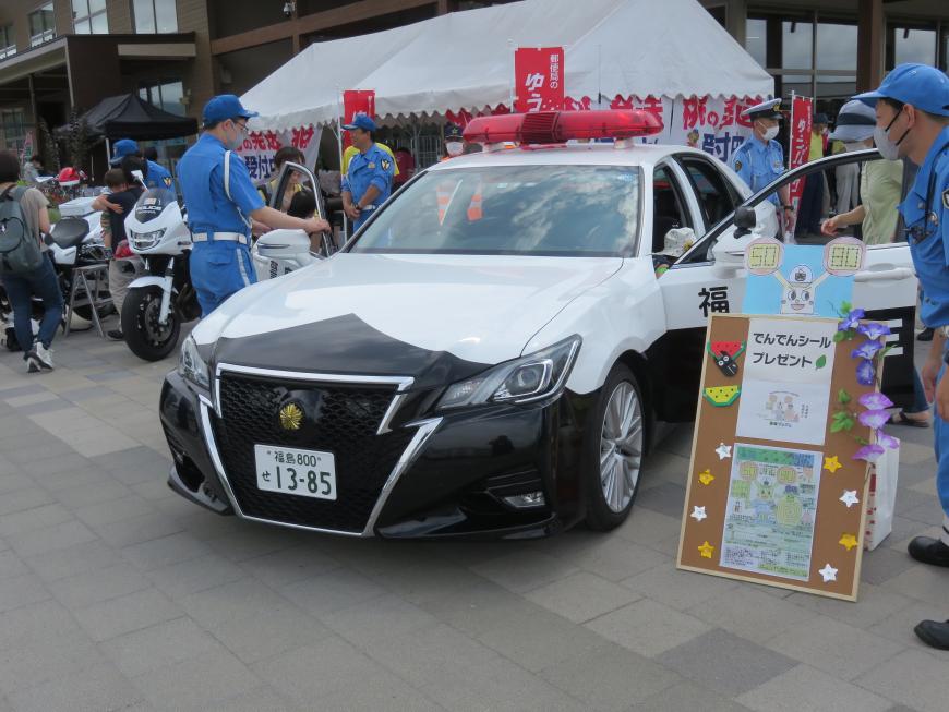 白いテントの前にパトカーや白バイが展示され、複数の警察官が試乗体験の対応をしている様子の写真