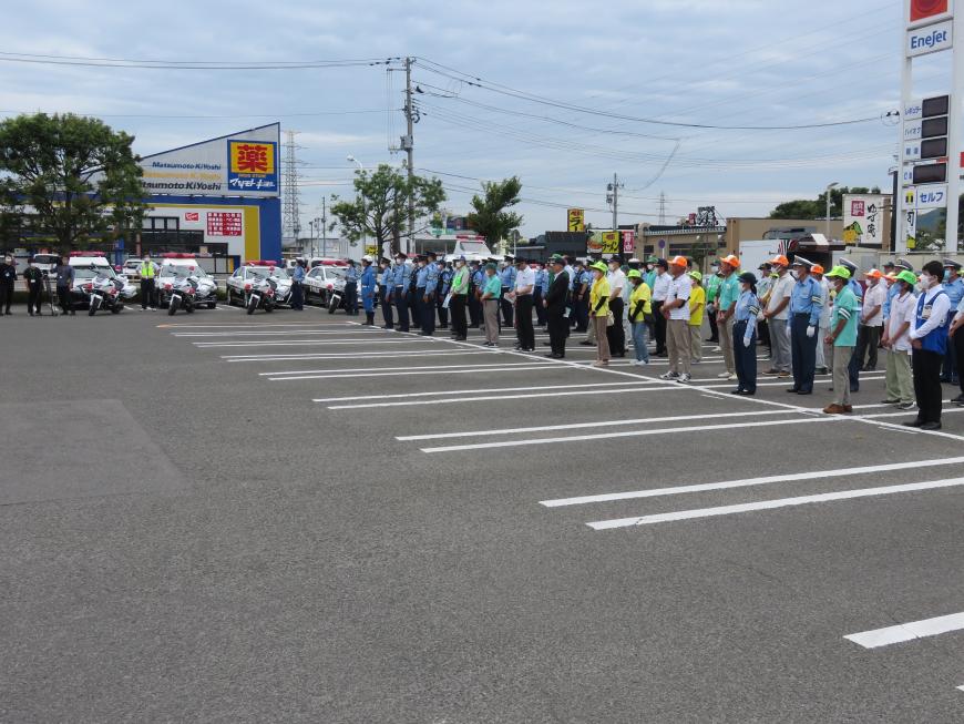 広い駐車場にパトカーや白バイが並び、大勢の警察官や関係団体の人々が整列している写真