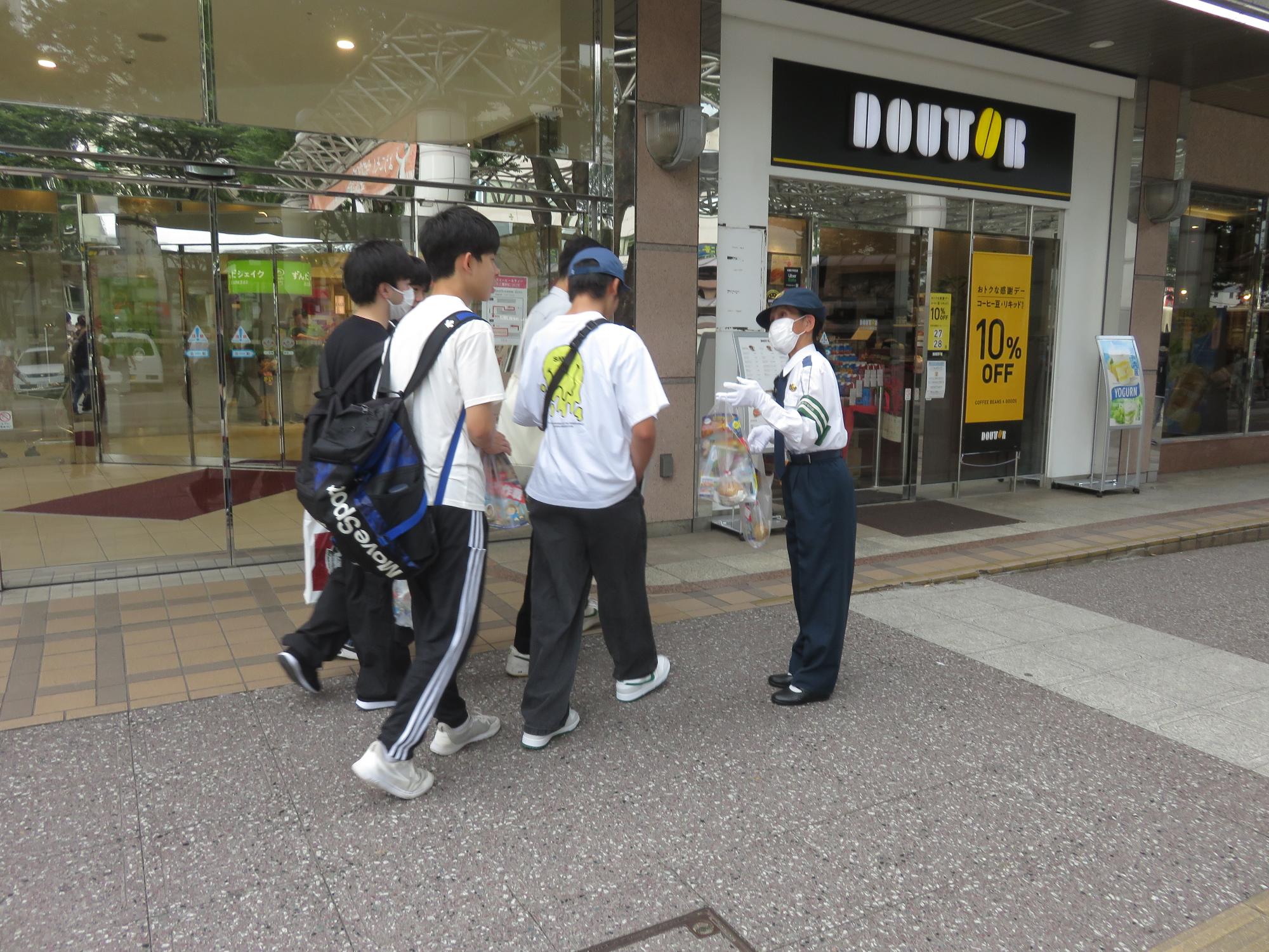 制服を着用した交通教育専門員が、駅前広場利用者へ啓発グッズを渡し、呼びかけている様子