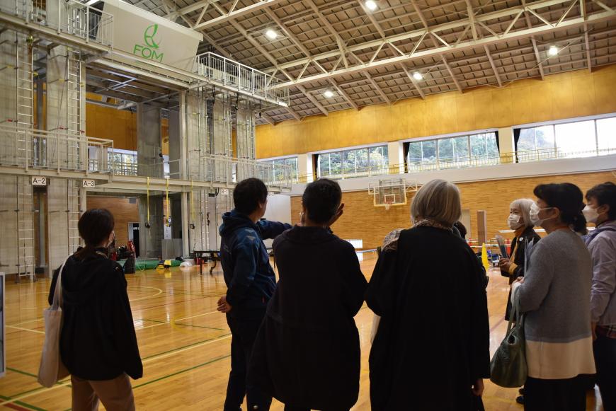 体育館のような室内で参加者の方が係の方の話を聞いている写真
