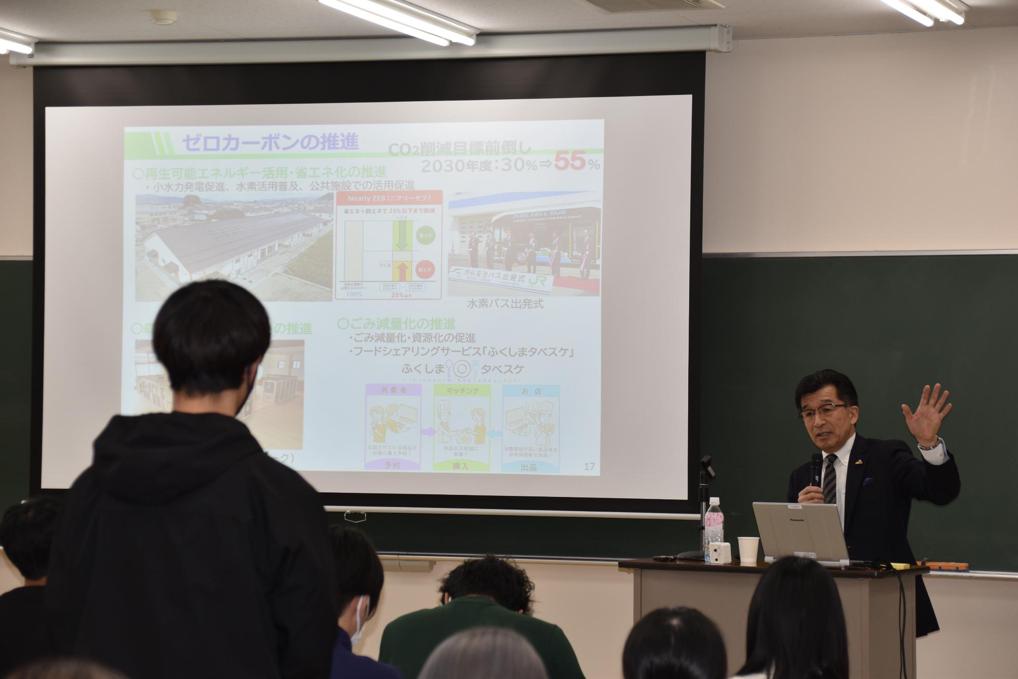 椅子から立ち上がった黒いパーカーを着た人が市長に質問を行っている様子の写真