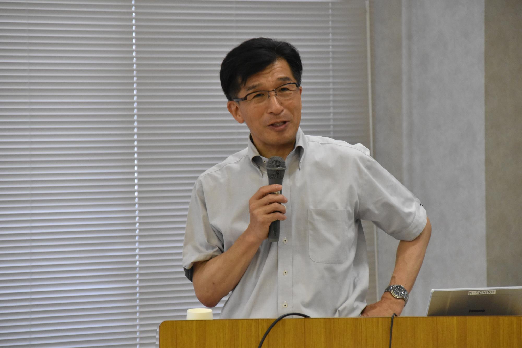 薄いグレー色のシャツを着た市長が右手にマイクを持ち話をしている様子をアップで撮影した写真