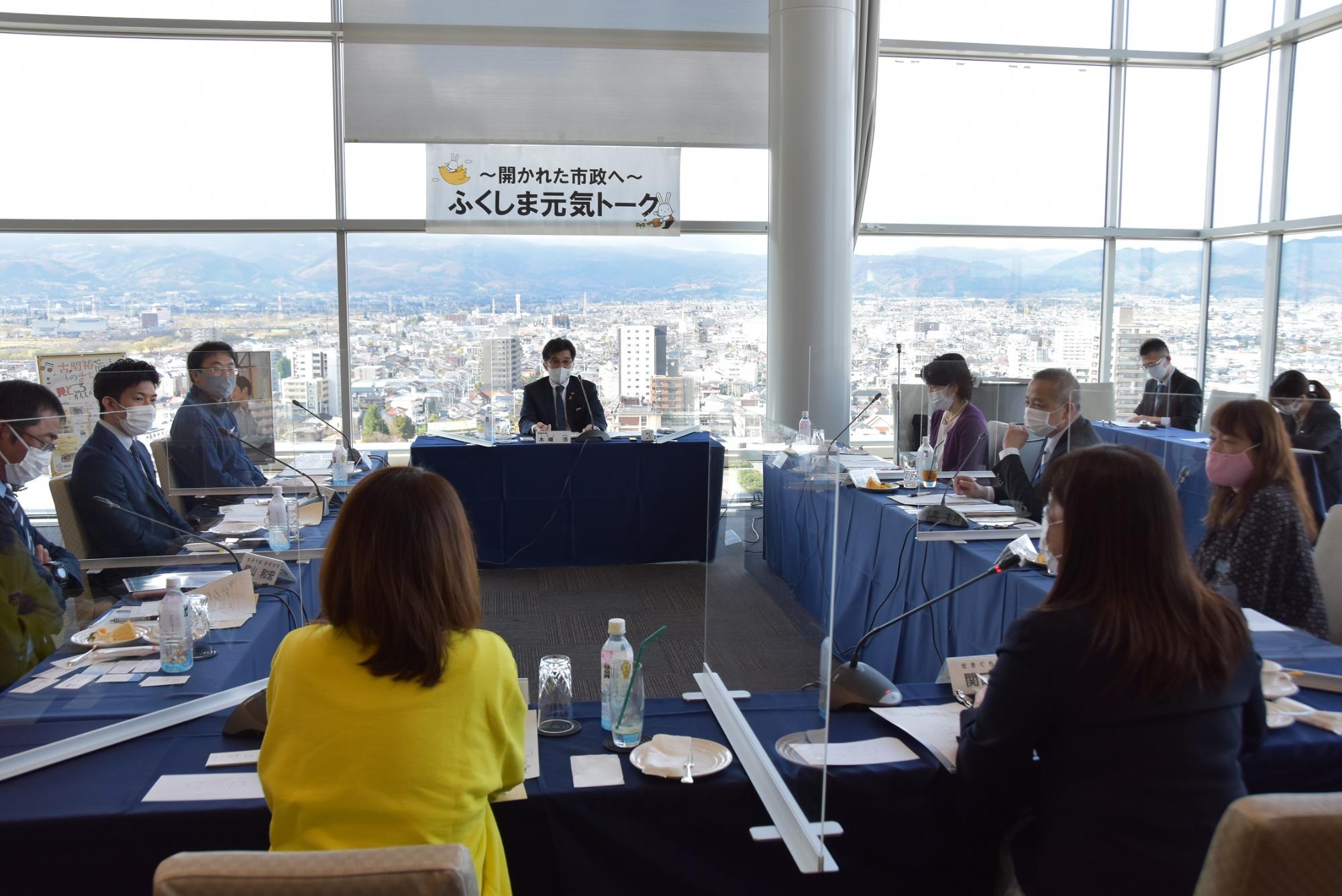 ロの字型に机と椅子が設置され、各自席にマイクが置かれ、参加者の方々が意見交換会を行っている写真