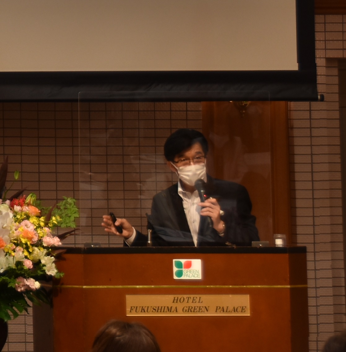 パーテーションが設置された壇上に立つ市長が、右手にマイクを持ち話をしている様子をアップで撮影した写真