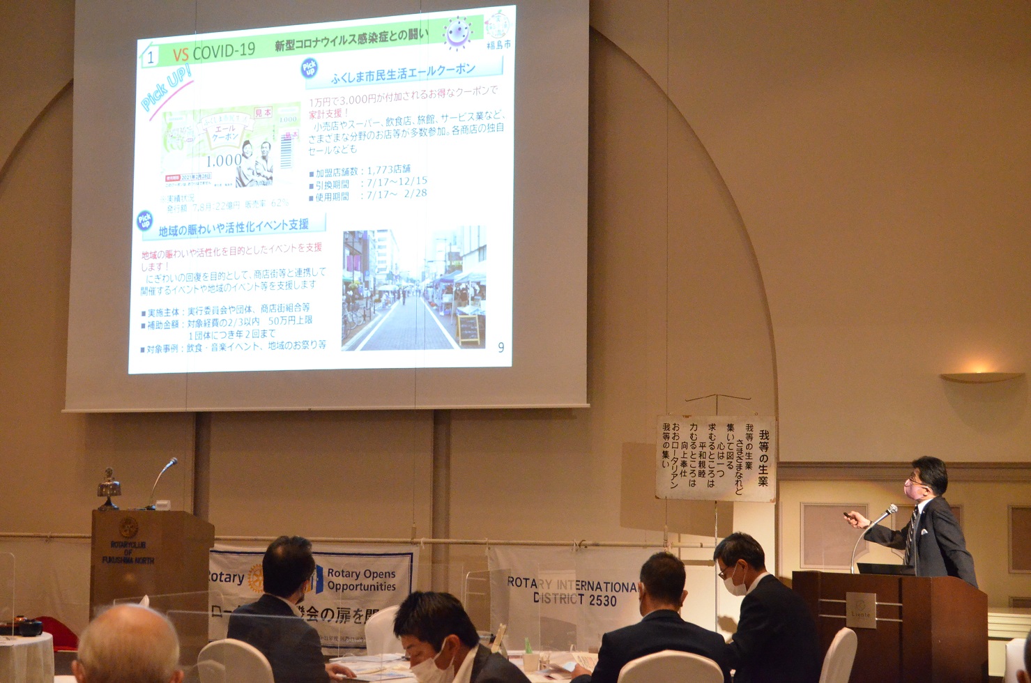 資料が映し出されたスクリーンが設置された右側に立つ市長が参加者に向かって話をしている様子の写真