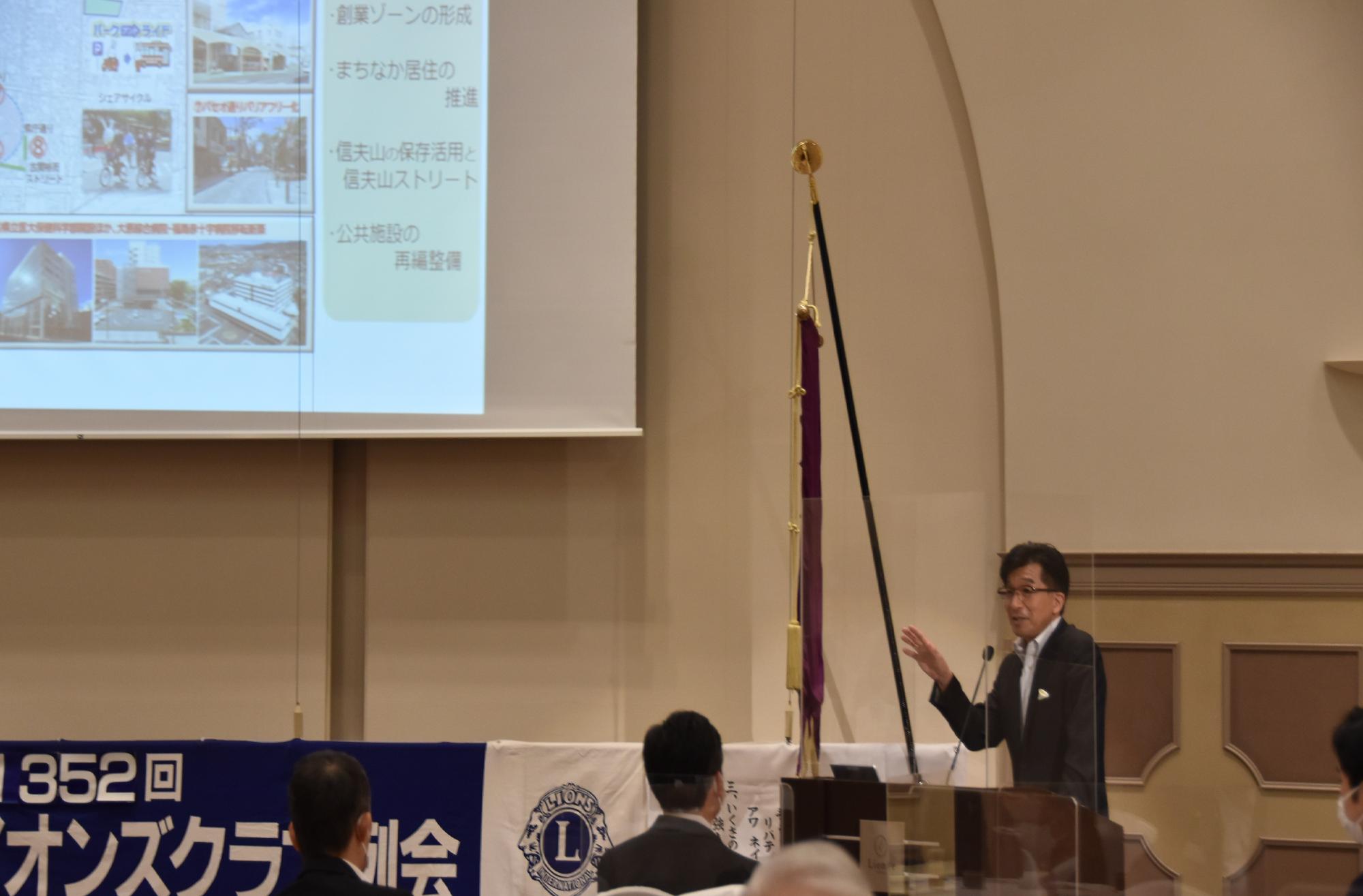 資料が映し出されたスクリーンの右下の檀上に立つ市長が参加者に向かって話をしている様子の写真