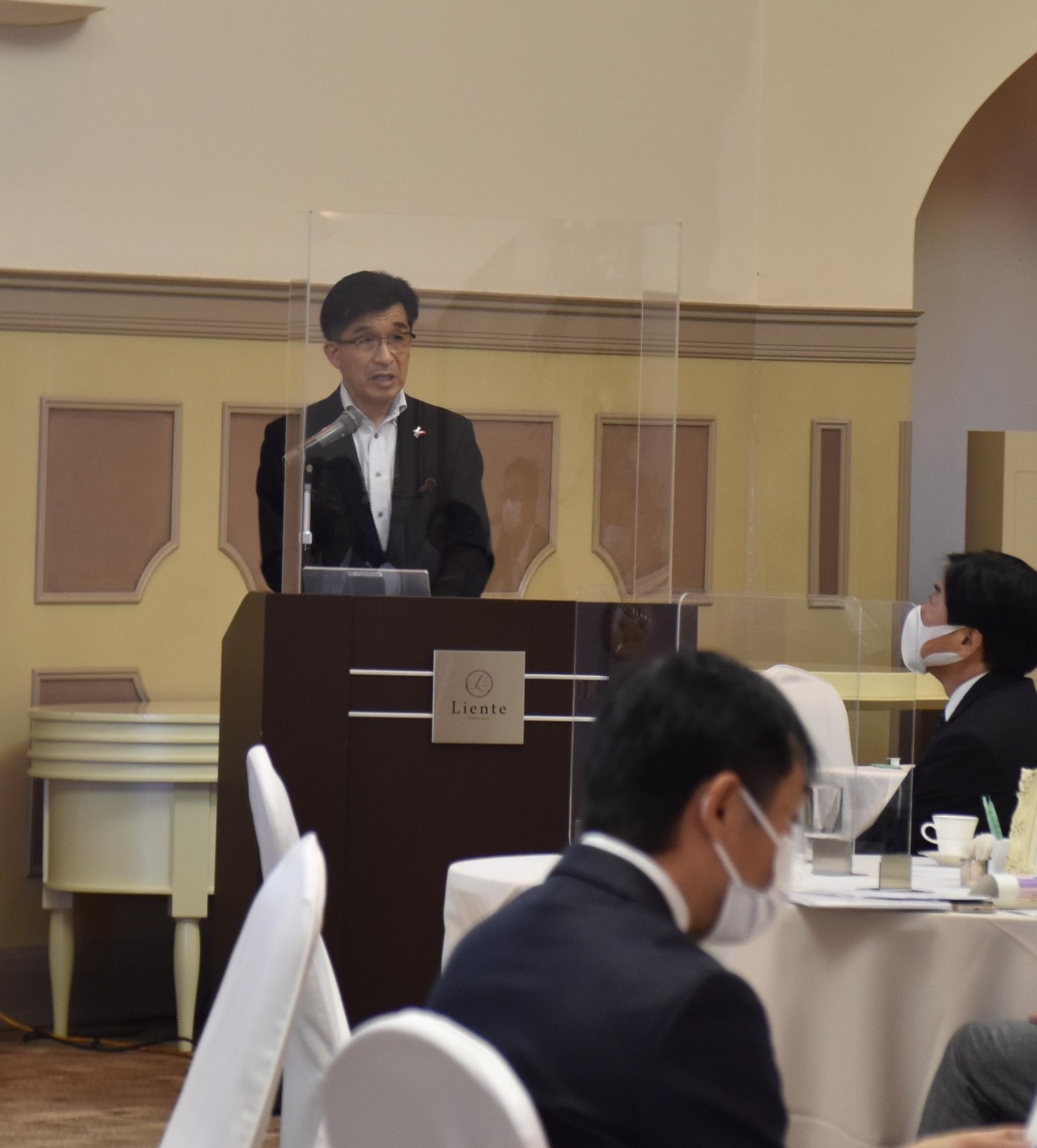 パーテーションが設置された壇上で市長が話を行っている様子をアップで撮影した写真