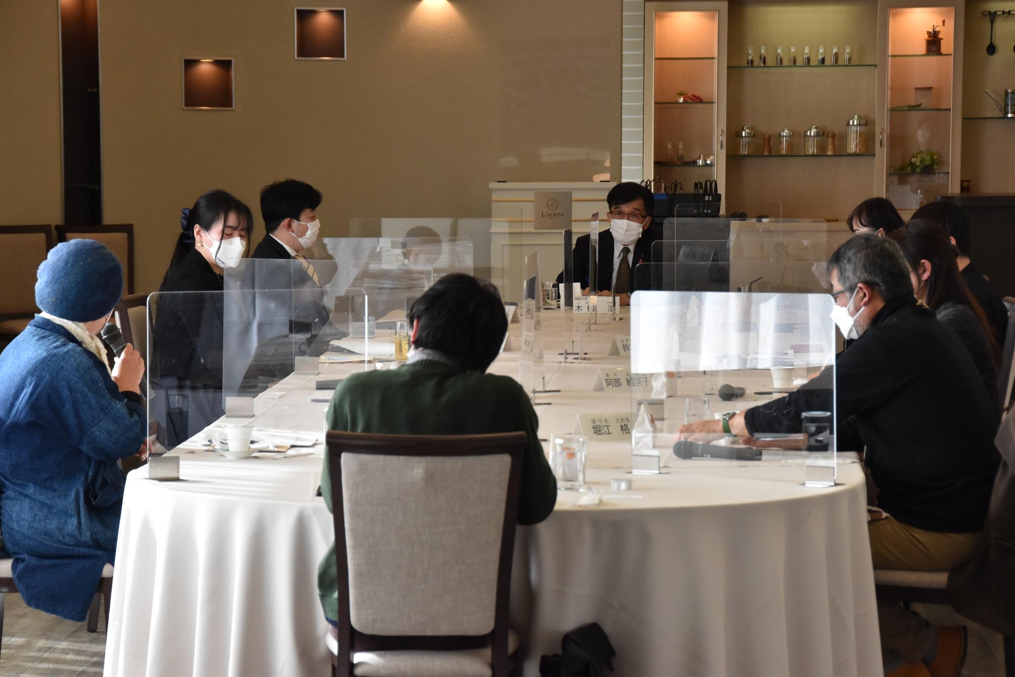 大きな楕円形のテーブルの席に参加者が座り、意見交換会が行われている写真