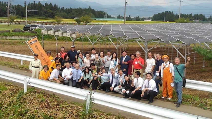 畑に太陽光発電が設置され、そのまえの道路に参加者達が並んで記念撮影をしている写真