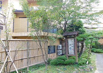 竹垣で仕切られた敷地内に木々が生えている「 土湯温泉はるみや旅館 」の入り口付近の写真