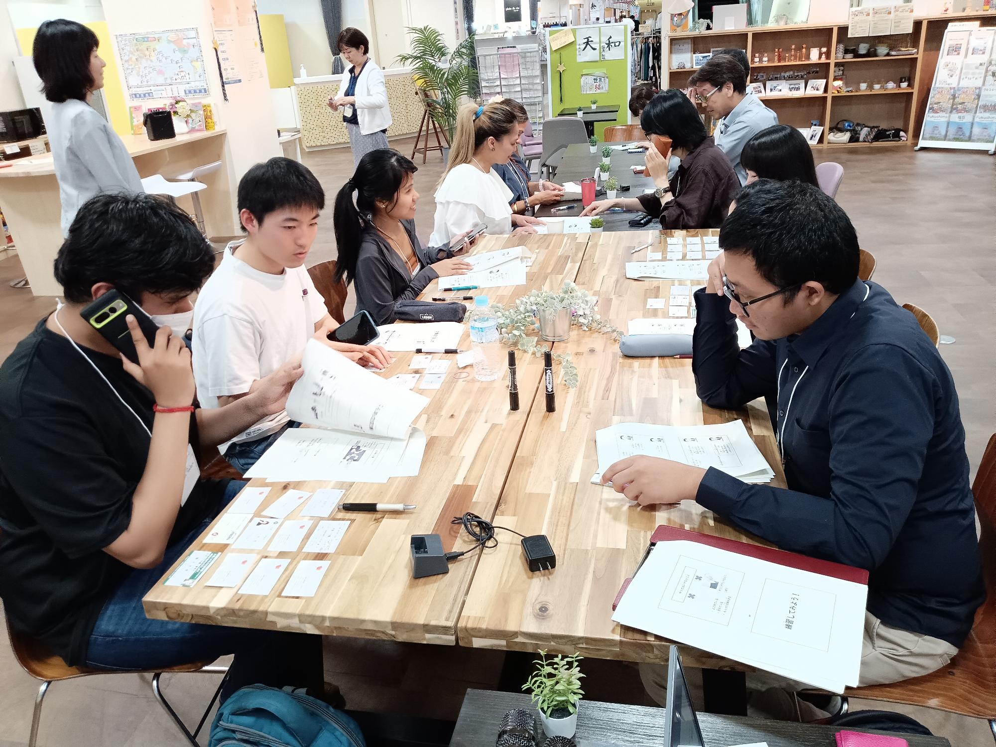 女性講師が見守るなか、向かい合って座っている参加者が資料を見ながら電話のかけ方の練習を行っている講座の様子の写真