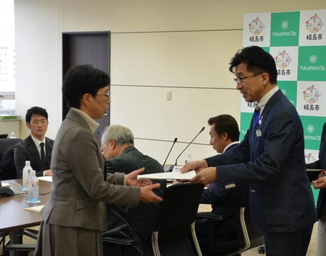 後ろに関係者が着席し市長が男性に委嘱状を渡す様子の写真