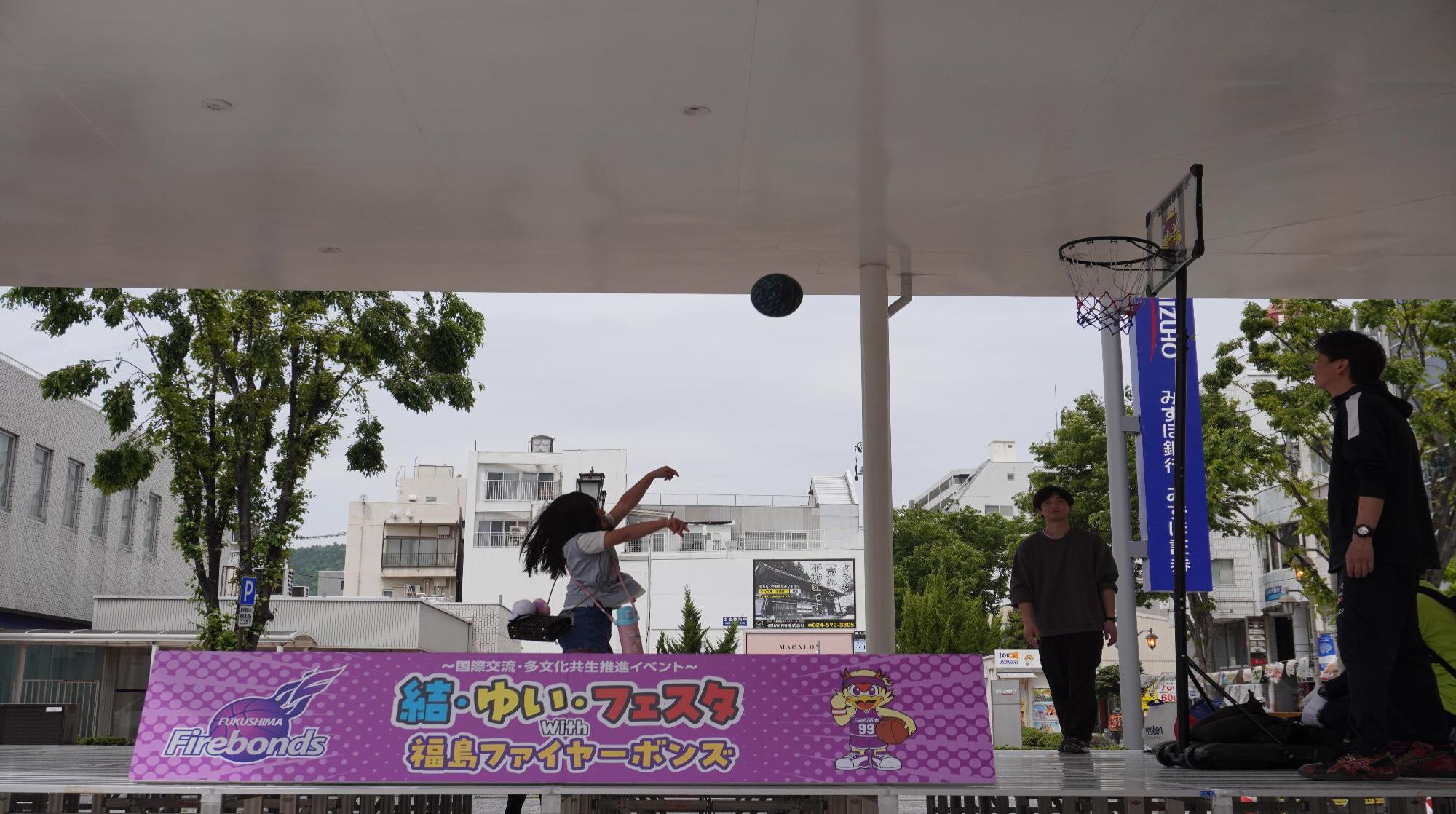 ステージでのフリースローチャレンジで、女の子がバスケットゴールに向かってボールを投げる様子