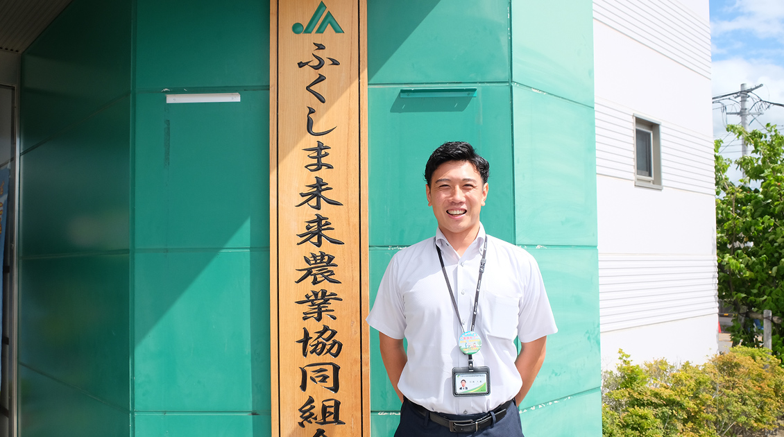 ふくしま未来農業協同組合の建物を背景に羽賀さんの笑顔の写真