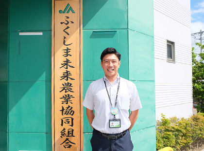 ふくしま未来農業協同組合の建物を背に笑顔で写っている羽賀さんの写真（羽賀 大貴さんのページへリンク）
