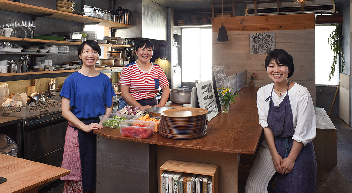 食材やお皿が置かれた大きなテーブルを囲んだ「食堂ヒトト」のスタッフと近藤 仁美さんの写真