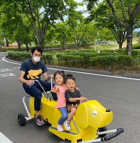 お父さんが運転する犬のおもしろ自転車の前に乗った子供達が喜んでいる写真