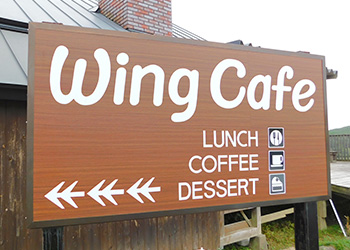 建物の前に設置された茶色地に白文字で「 Wingcafe 」と書かれた看板の写真