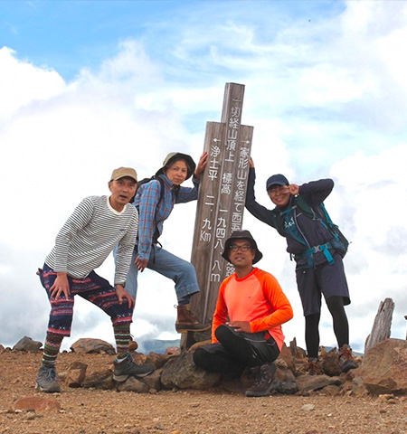 3本の標柱の周りに立つ登山仲間3人と宮司 君香さんの写真