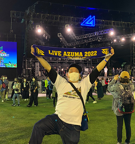 野外のイベントで「LIVE AZUMA」のタオルを持ち嬉しそうな水野 圭悟さんの写真