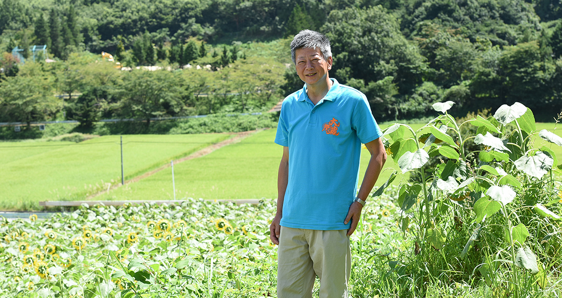 緑豊かな自然に囲まれた永井 康統さんの笑顔の写真