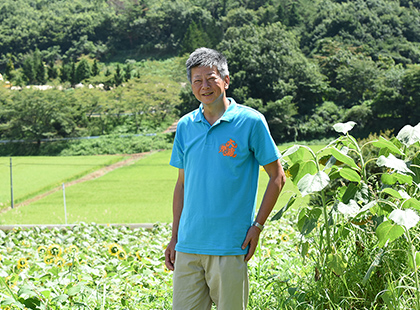緑豊かな自然に囲まれた永井 康統さんの笑顔の写真（永井 康統さんのページへリンク）