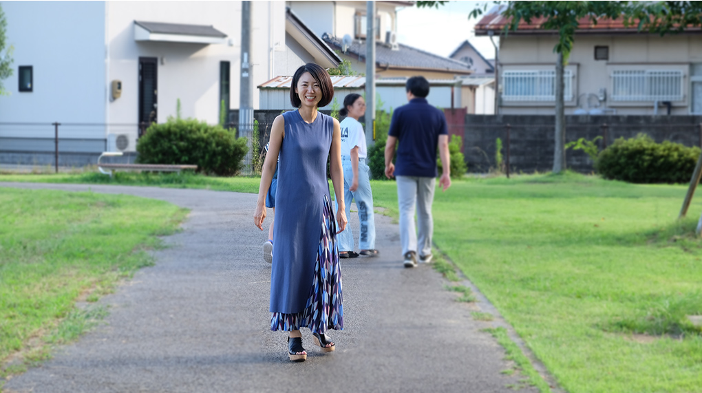 公園内の遊歩道を散歩する家族と間隔をあけて笑顔で振り返る中島 明日香さんの写真