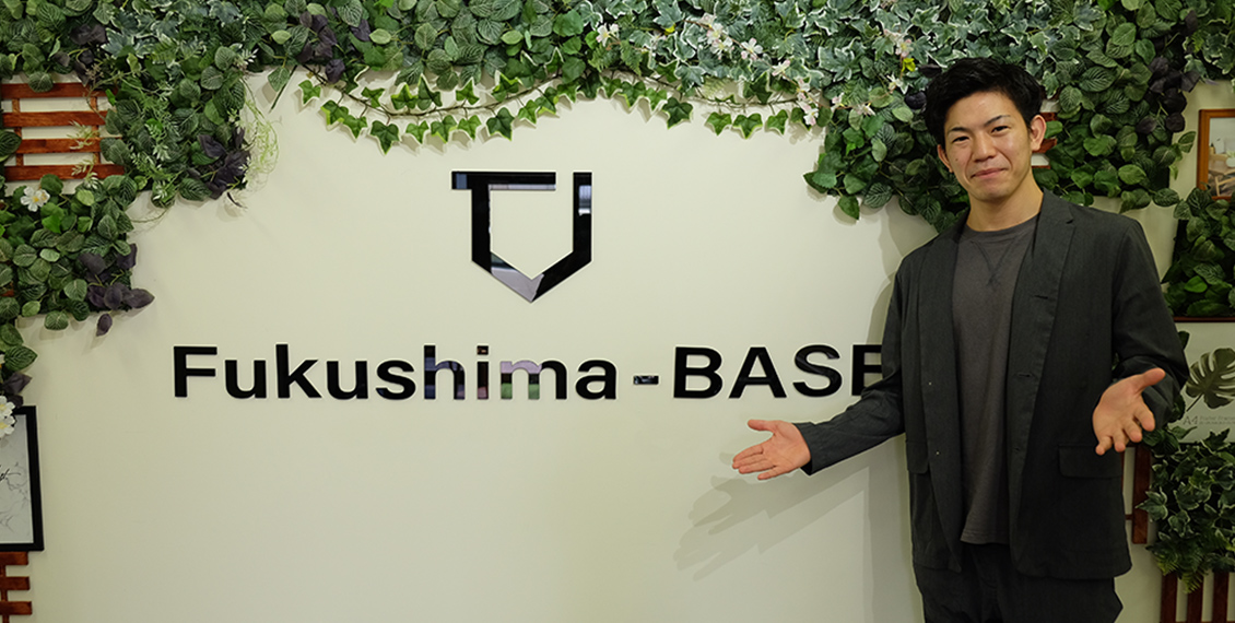 社名の「Fukushima-BASE」とロゴが書かれた建物の前で中野 友登さんが両手を広げている写真