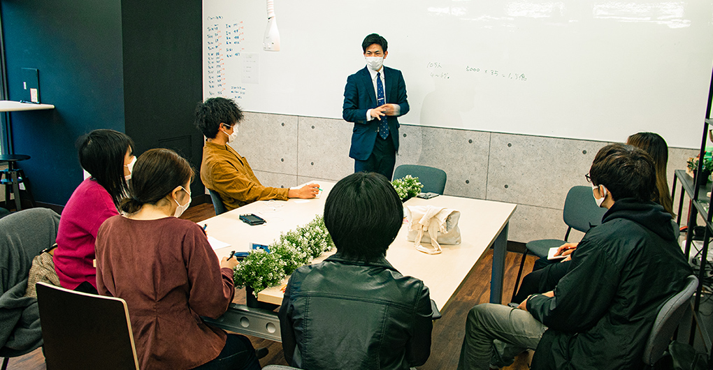 ホワイトボードの前に立つ中野 友登さんが話をするのを参加者が席に座り聞いている写真