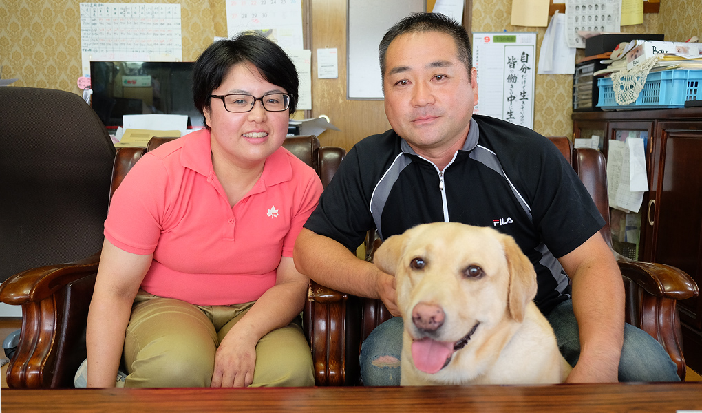 事務所内の椅子に座っている大内さん夫婦と飼い犬の写真