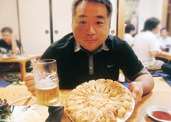 右手にビール、左手に丸い皿に盛られた焼き餃子を持った大内 徹也さんの写真