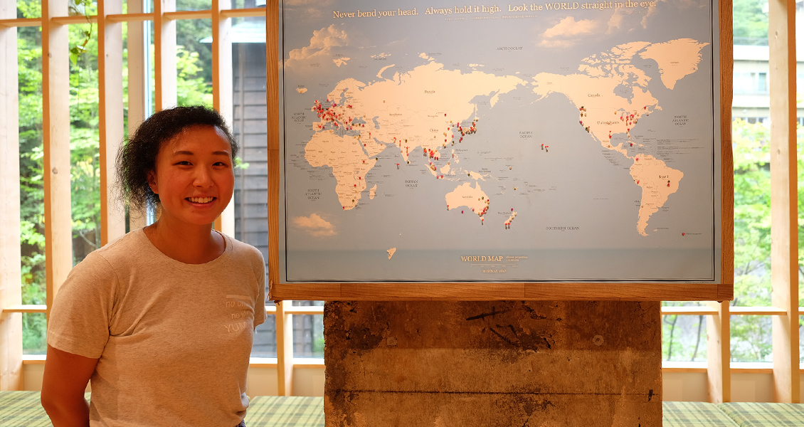 世界地図のパネルの横にパクさんが立っている写真