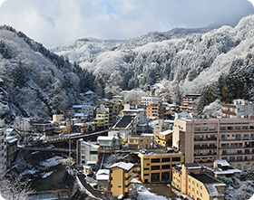 遠くの山々に雪が積もり、街にも雪が残る土湯温泉の街並みの写真