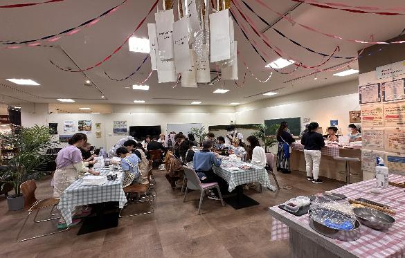 エプロンを付けた30名ほどの人が、自分たちで作った料理を食べている様子。