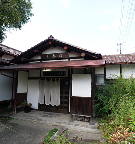 入り口に暖簾が下がっているレンガ色の屋根の如春荘の外観写真