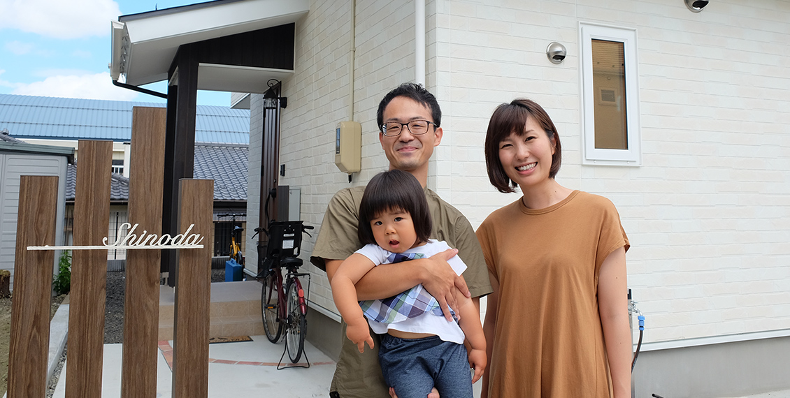 白壁のマイホームの前で女の子を抱っこした篠田さんと奥さんの3人家族の写真