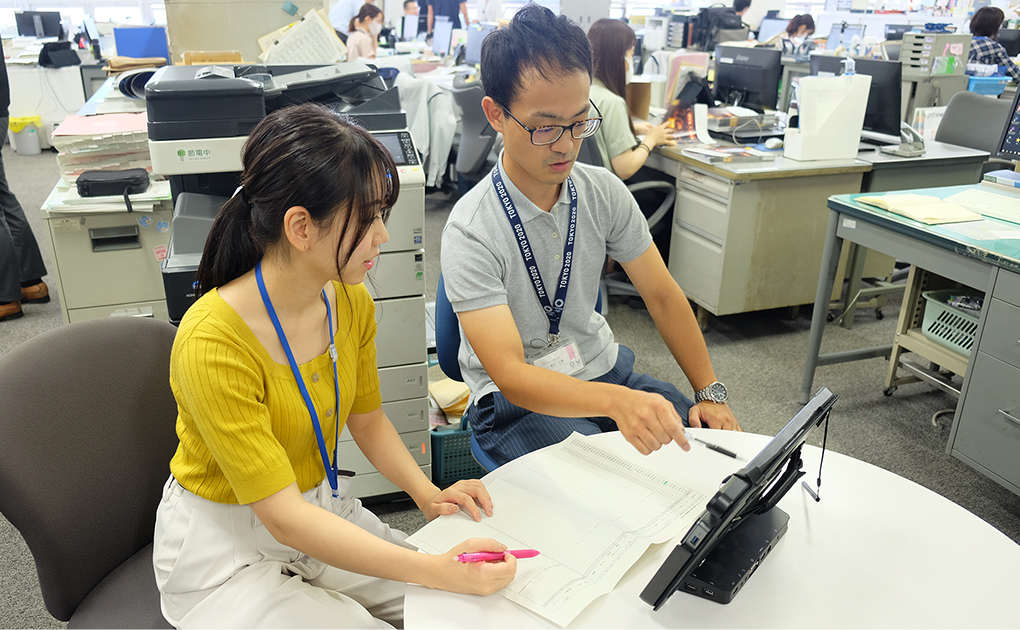 白い丸机の席に座った女性と篠田 大輔さんがモニターを指している業務中の様子の写真