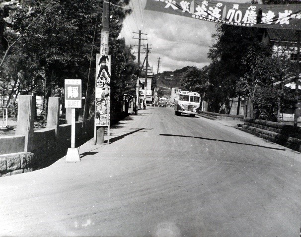 左側に電柱が等間隔に並んでいる通りをバスが走っている県庁通りを写した白黒写真