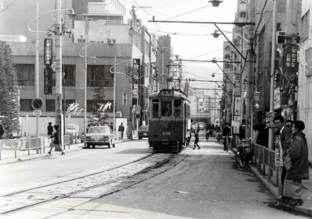両側に建物が立ち並ぶ間に通っている1本の道の中央に路面電車が走っている白黒写真