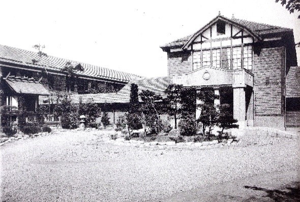 中央にある円形の花壇に植えられた植栽の奥に、大きな2階建ての建物と、横長の建物が左側に建っている福島県師範学校の白黒写真