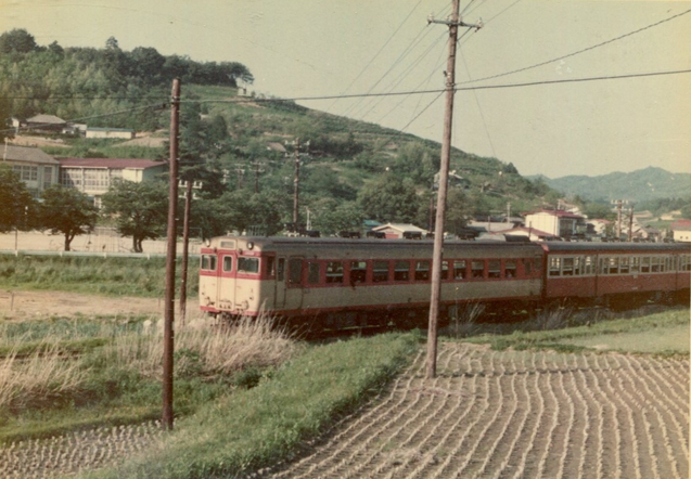 田園を走る赤とクリーム色をした列車の写真