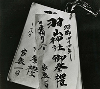 筆で文字が書かれた長方形の白い紙が、右上の角で紐で閉じられている金沢の羽山ごもり託宣記録の写真（福島市の文化財 -重要有形民俗文化財 2件-のページへリンク）